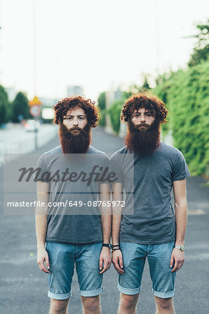Portrait of identical adult male twins with red hair and beards on sidewalk