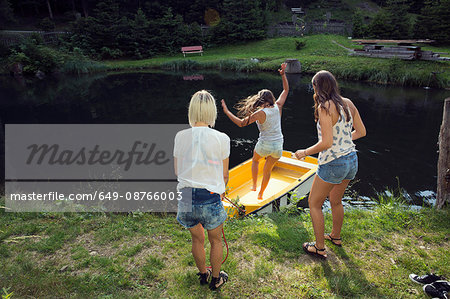 Three adult female friends jumping into rowing boat on lake, Sattelbergalm, Tirol, Austria