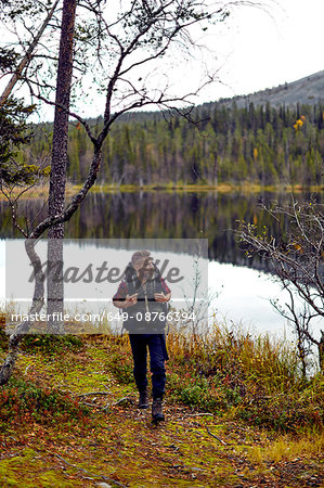 Hiker walking by lake, Kesankijarvi, Lapland, Finland