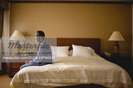 Man sitting on a bed looking thoughtful.