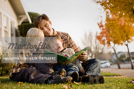 Father and sons sitting on lawn reading stories.