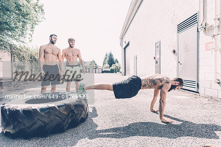 Young male cross trainer doing push-ups from tyre outside gym