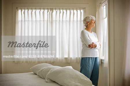 Elderly woman looking through bedroom window.