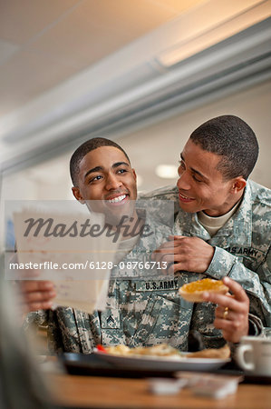 Young soldier looks over his friend's shoulder as he reads a  letter during breakfast.