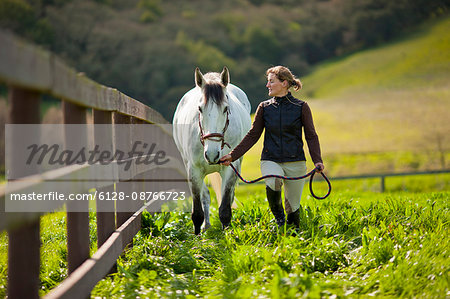 Young woman leading a horse through a grassy paddock on a farm.