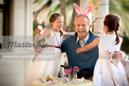 Grandfather hugging granddaughters at tea party.