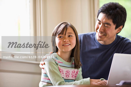 Father and daughter smile while working on a laptop together.