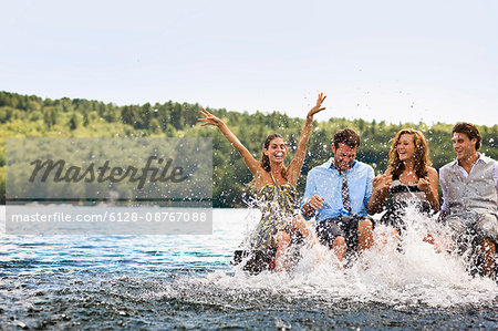 Group of friends sitting on a jetty,  splashing in the lake with their legs.