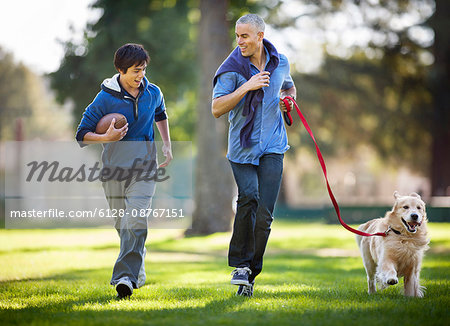 Smiling mid adult man and his son having fun jogging together in the park with their dog.