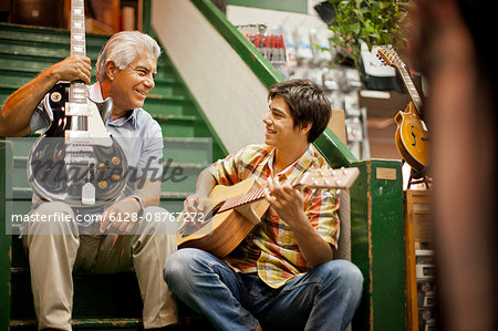 Smiling senior man playing guitar with his teenage grandson.