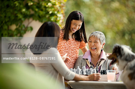 Happy senior woman playing a game of chess with her adult daughter and young granddaughter.