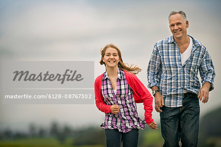 Portrait of a smiling father and daughter running side by side.