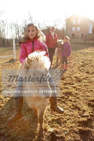 Young girl riding pony, mother and sister watching from behind