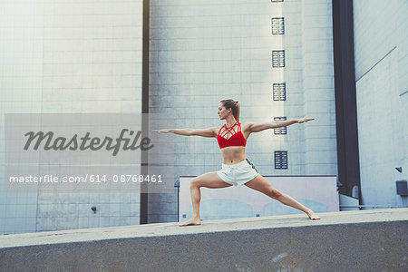 Young woman outdoors, standing on wall in yoga position