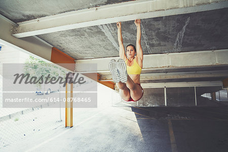 Young woman exercising outdoors, hanging on structural beam