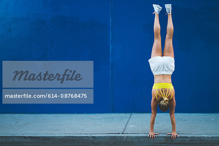 Young woman doing handstand outdoors in front of blue wall
