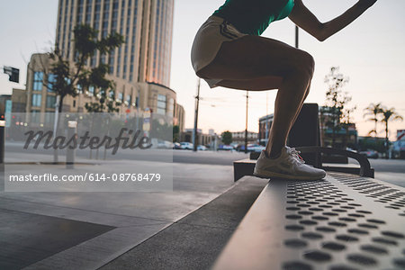 Young woman exercising outdoors, stepping up onto bench
