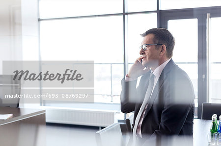 Side view of mature businessman talking on mobile phone at office