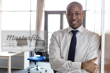 Portrait of smiling young businessman with arms crossed leaning on cupboard in office