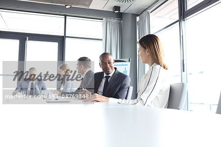 Young businessman discussing with female colleague in board room