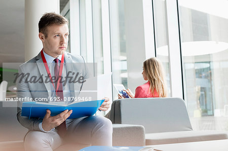 Thoughtful businessman holding file while sitting at lobby in convention center