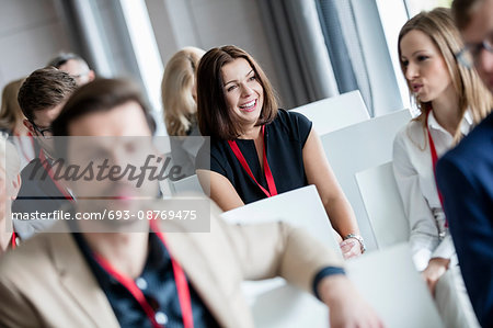 Happy businesswoman sitting with colleagues in seminar hall