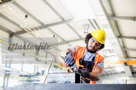 Young manual worker using grinder on metal in factory