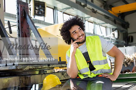Young manual worker talking on mobile phone in metal industry