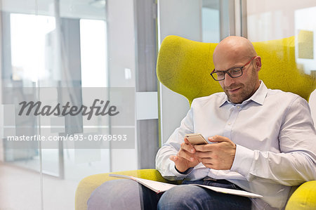 Mid adult businessman using mobile phone while sitting on chair at office