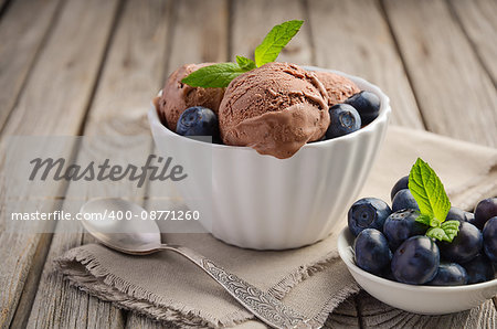 Chocolate ice cream with blueberries in white bowl on rustic wooden background, selective focus, horizontal permission, copy space