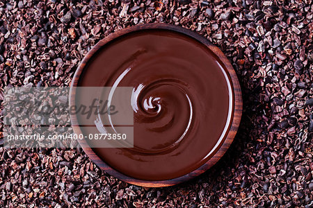 Bowl of melted chocolate on a crushed raw cocoa beans, nibs background. Copy space. Top view