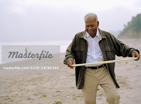 Senior man playing with a hula hoop at the beach.