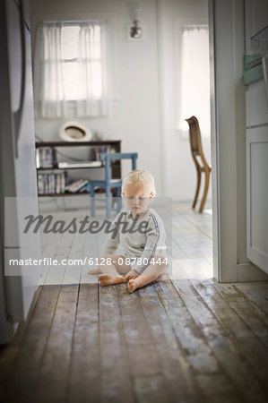 Young toddler sitting on a wooden floor inside his home.