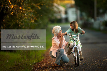 Little girl learning to ride her bicycle with the help of her grandmother.