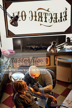 Woman getting her arm tattooed at a tattoo parlour.