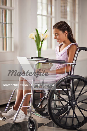 Young girl sitting in wheelchair typing on laptop.