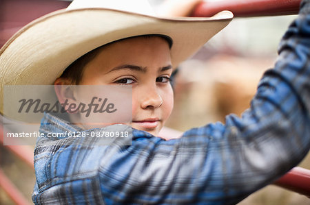 Portrait of young cowboy standing on fence.