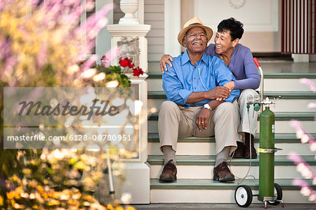 Senior woman sitting on the staircase and hugging her happy husband with nasal tubes.