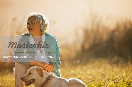 Portrait of mature woman crouching on the field with her dog.