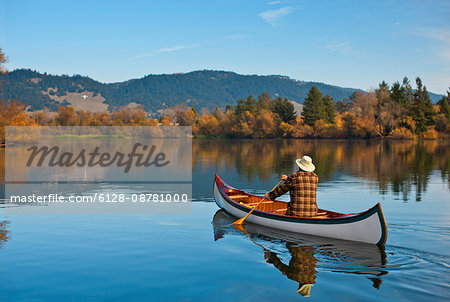 Man canoeing across a tranquil scenic lake.