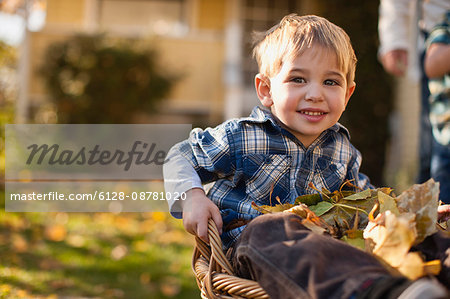 Portrait of boy sitting in a basket filled with leaves.