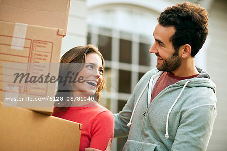 Mid-adult couple carry moving boxes.