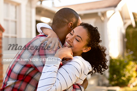 Mid-adult couple hugging in front of their new home.