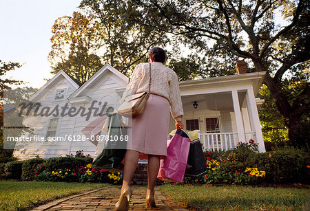 Senior woman walking up the path to her house while carrying shopping bags.