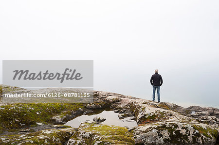Sweden, Man standing on edge of rock and looking at sky