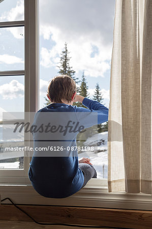 Norway, Oppland, Hafjell, rear view of boy (12-13) sitting in window