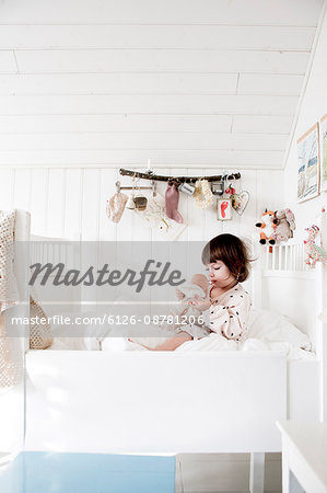 Sweden, Small girl (2-3) sitting in bed and embracing doll