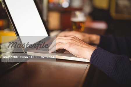 Mid section of man using laptop at bar counter