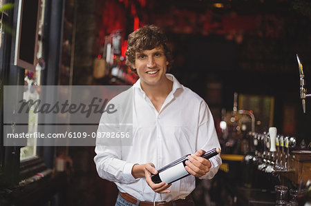 Portrait of bar tender holding a bottle of wine at bar