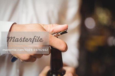 Close-up of bartender opening a beer bottle at bar counter